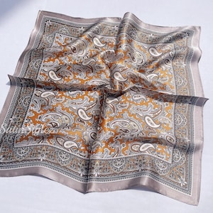 May include: A brown and gray paisley patterned silk scarf with a decorative border.