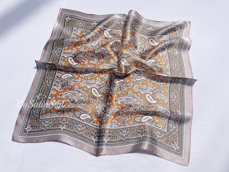 May include: A brown and gray paisley patterned silk scarf with a decorative border.