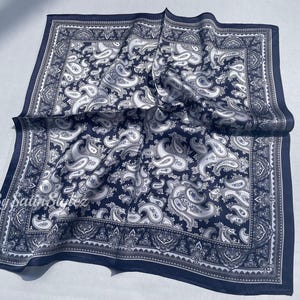 May include: A navy blue paisley bandana with a white paisley pattern. The bandana is folded and has a fringed edge.