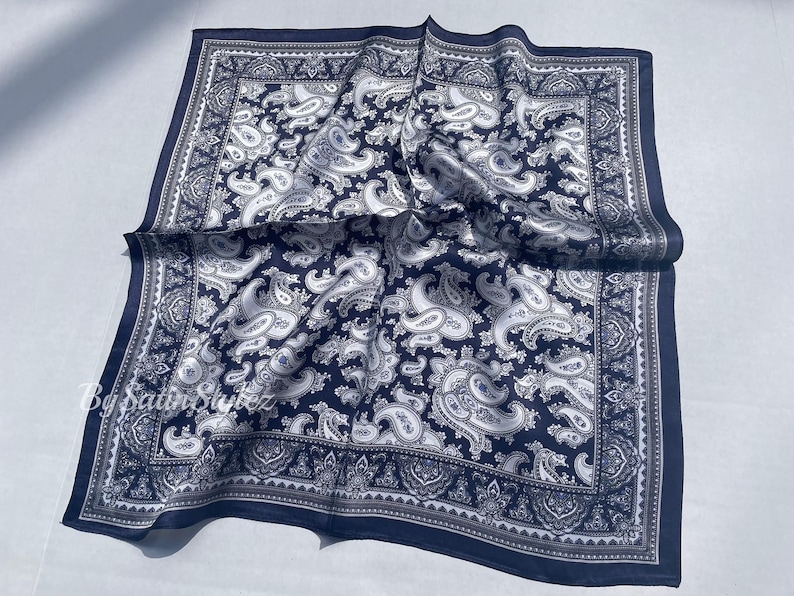 May include: A navy blue paisley bandana with a white paisley pattern. The bandana is folded and has a fringed edge.