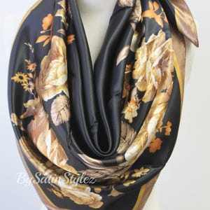 May include: A black satin scarf with a gold floral print. The scarf has a brown border.