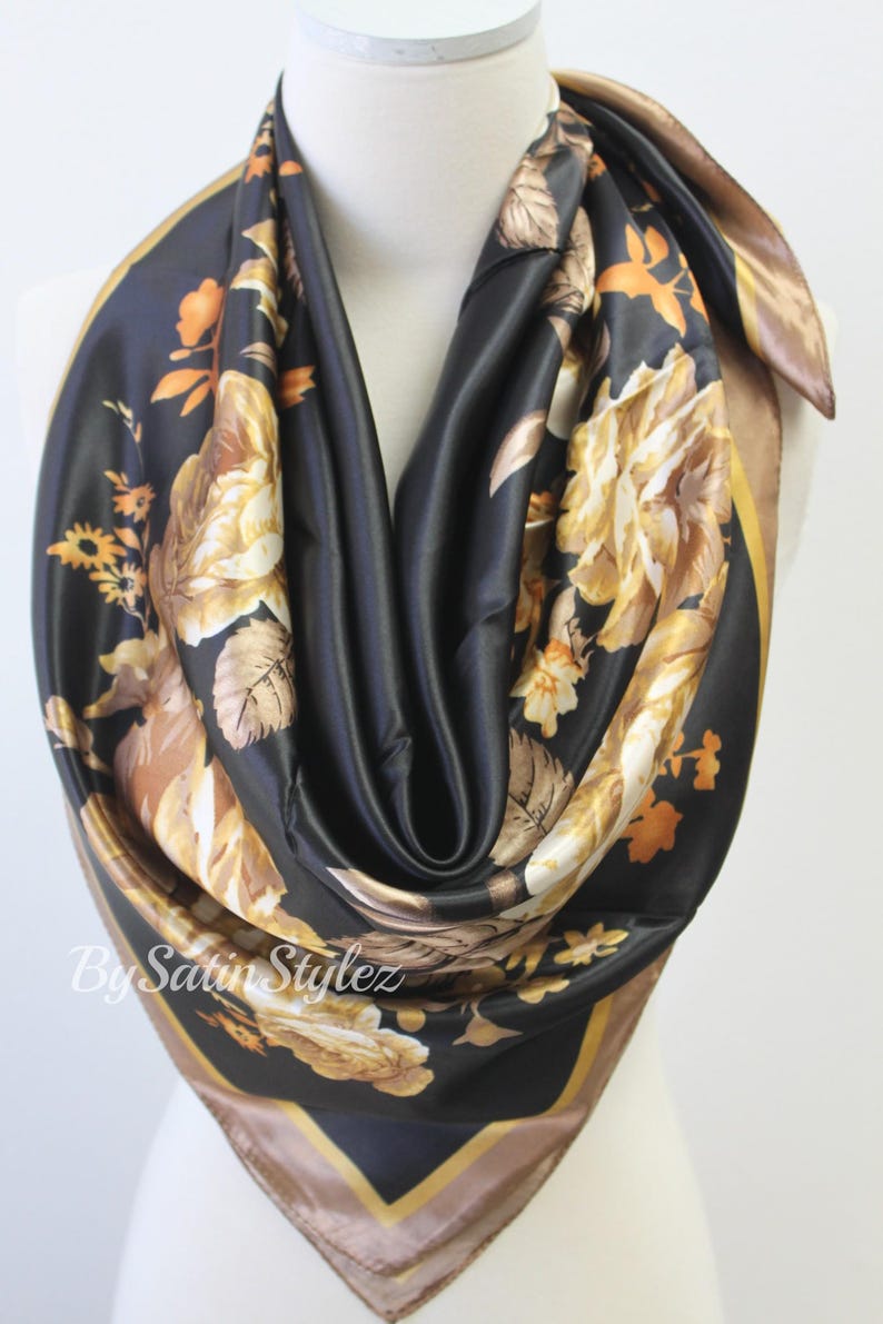 May include: A black satin scarf with a gold floral print. The scarf has a brown border.