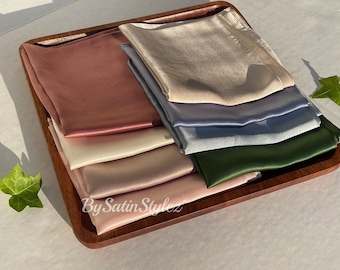 Pode incluir: Um conjunto de oito lenços de cetim em várias cores, incluindo rosa, bege, verde e azul, dispostos em uma bandeja de madeira. Os lenços são feitos de cetim macio e luxuoso, perfeitos para adicionar um toque de elegância a qualquer roupa.