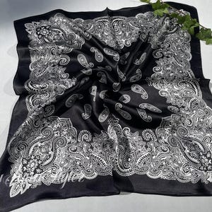 May include: Black satin bandana with a white paisley pattern. The bandana is folded and laid flat on a white surface.