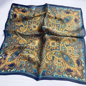 May include: A blue silk pocket square with a paisley pattern in shades of gold, brown, and green.