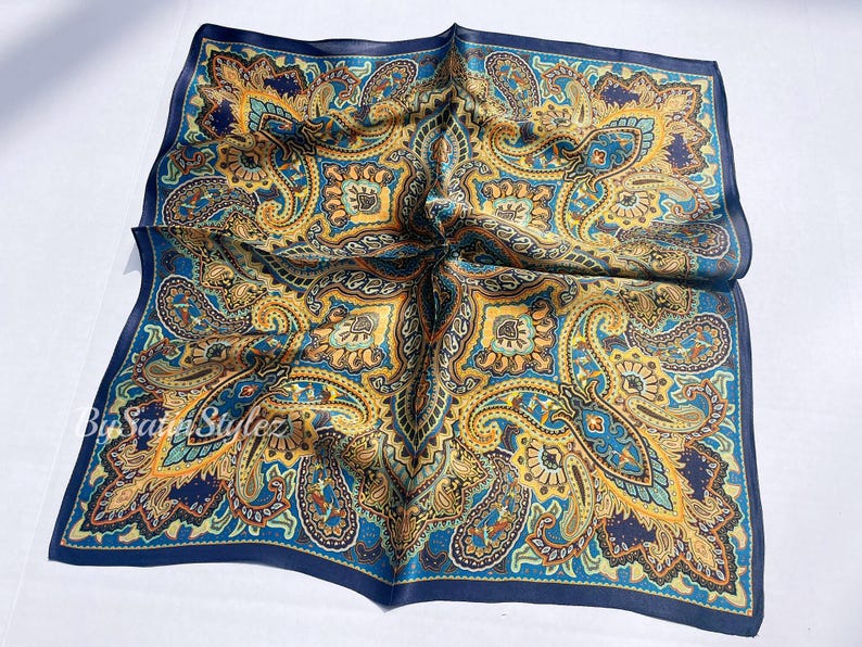 May include: A blue silk pocket square with a paisley pattern in shades of gold, brown, and green.