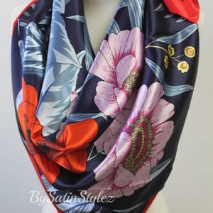 May include: A navy blue satin scarf with a floral print featuring red, pink, and yellow flowers. The scarf has a red border and the text "By Satin Stylez" is printed on the bottom.