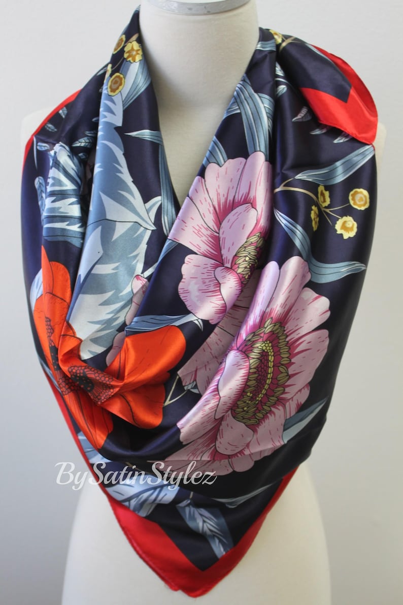 May include: A navy blue satin scarf with a floral print featuring red, pink, and yellow flowers. The scarf has a red border and the text "By Satin Stylez" is printed on the bottom.