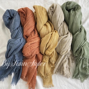 May include: Five different coloured scarves made of a soft, woven fabric. The scarves are in shades of blue, orange, yellow, beige, and green.
