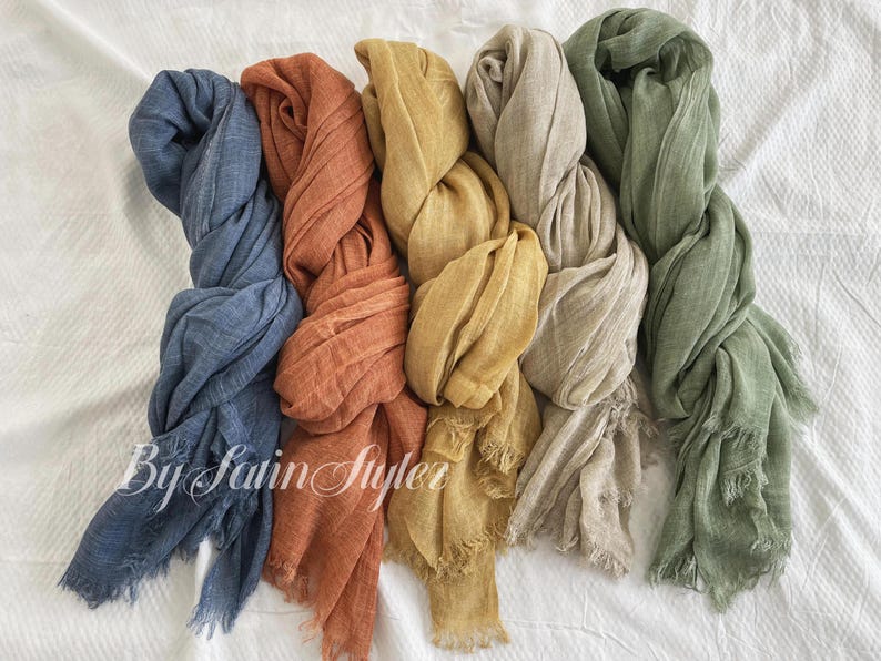 May include: Five different coloured scarves made of a soft, woven fabric. The scarves are in shades of blue, orange, yellow, beige, and green.