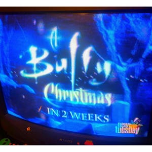 以下が含まれることがあります： 青いテレビ画面に、光る書体で「Buffy Christmas」のタイトルが表示されています。「IN 2 WEEKS」というテキストが下にあり、「new tuesday」のロゴがあります。