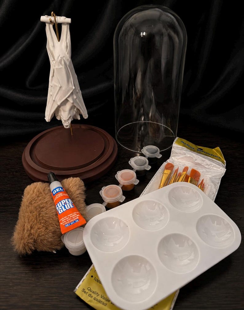 May include: A craft kit with a white sculpture, a glass dome, paint pots, paint brushes, a paint palette, and a tube of Super Glue. The kit includes a brown base and a small, furry item.