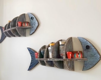 May include: Two wooden fish-shaped wall shelves painted in blue and grey. The shelves are stacked on top of each other and have small items on them.