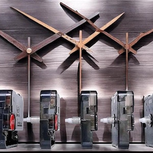 May include: Close-up of six black clock mechanisms with silver gears and a white background. The mechanisms are arranged in a row, with the first one on the left having a red and white dial. The mechanisms are used for DIY clock projects.