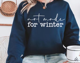 Puede incluir: Una sudadera de cuello redondo y manga larga en color azul marino oscuro con el texto blanco "not made for winter" impreso en el pecho en una combinación de letras cursivas y de bloque. La prenda tiene cuello y puños acanalados.