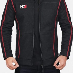 以下が含まれることがあります： 赤のアクセントが付いた黒いジャケット。袖と肩にストライプが入っています。スタンドカラーとフルジッパーが付いています。左胸には白と赤の「N7」パッチがあります。スタイリッシュなアウターウェアです。