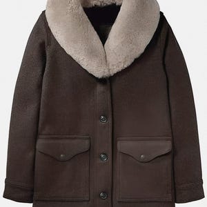 May include: A brown coat with a light tan shearling collar. The coat has two front pockets, a button-up closure, and a classic design. The coat is a medium length and appears to be made of a durable material.