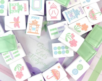 May include: A collection of white Mahjong tiles with various colorful illustrations, including flowers, umbrellas, and dragonflies. Some tiles have green accents, and some say "Joker". The tiles are scattered on a striped background.