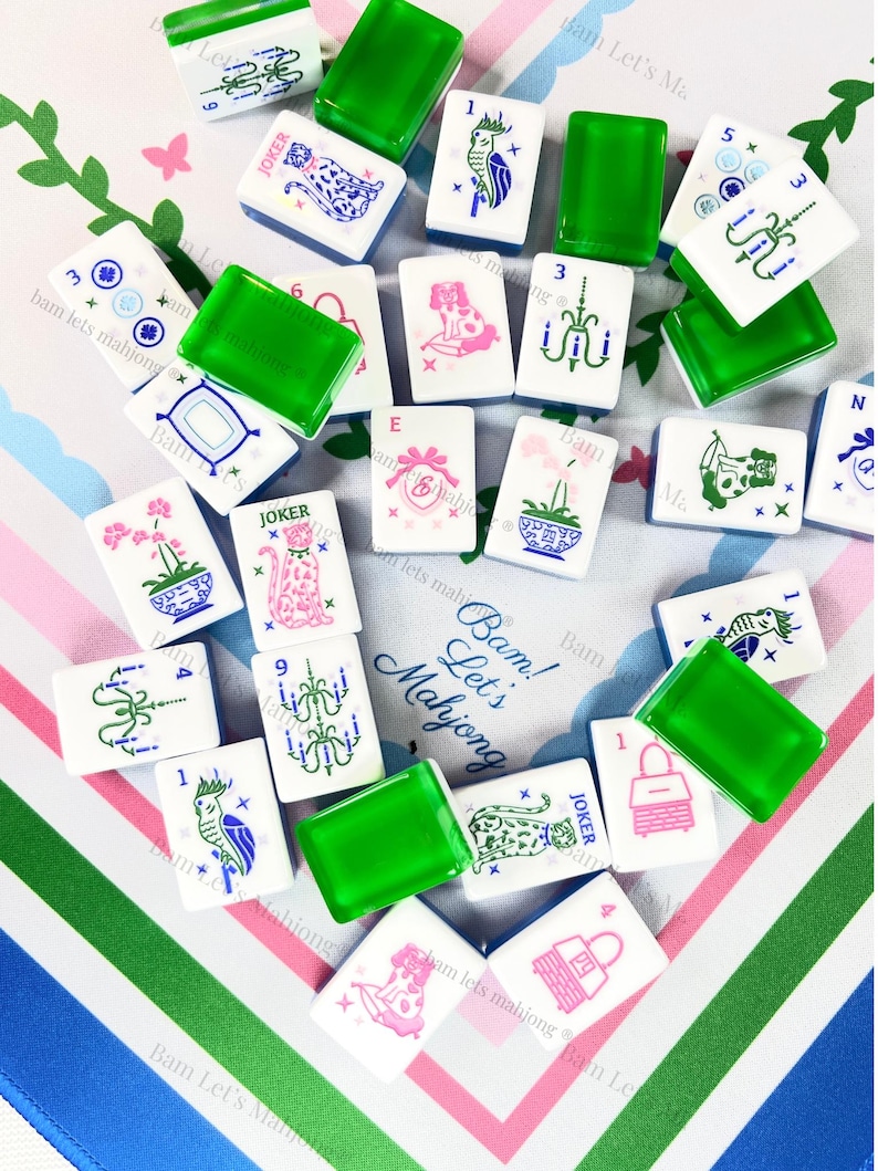 Pu&ograve; includere: Una collezione di tessere di Mahjong bianche con varie illustrazioni in rosa, blu e verde, tra cui fiori, animali e lampadari. Sono presenti anche pezzi rettangolari verdi. Il testo "Bam! Let's Mahjong" &egrave; visibile.