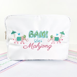 May include: White cosmetic bag with embroidered pink elephants, green umbrellas, and blue butterflies. The bag features the text "BAM! Let's Mahjong" in green and pink, with a gold zipper.