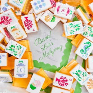 May include: A collection of white and orange Mahjong tiles with various colorful illustrations, including palm trees, coral, and seahorses. The text "Bam! Let's Mahjong" is visible on a green and white background.