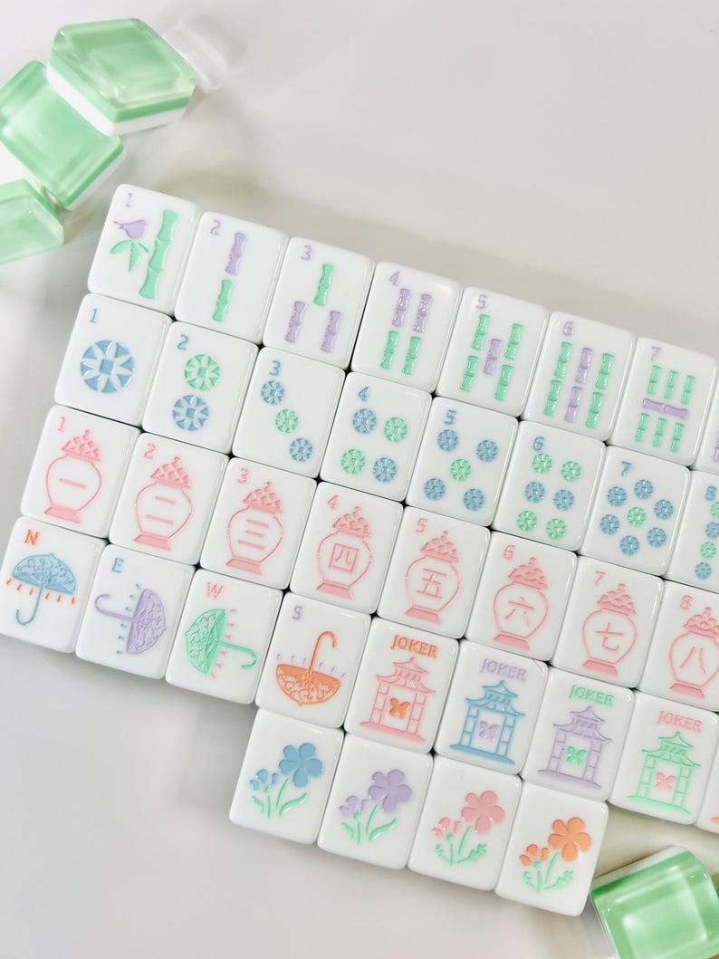 May include: A set of white Mahjong tiles with various colorful designs and numbers. The tiles feature illustrations of umbrellas, flowers, and pagodas in pastel colors. Some tiles have the word "JOKER".