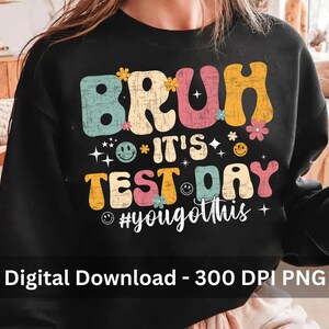 May include: Black sweatshirt with a retro-style graphic that says "Bruh it's test day #yougotthis". The graphic features colourful letters, flowers, and smiley faces.