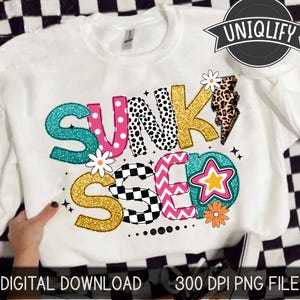 以下が含まれることがあります： 「Sunkissed」と書いてあるカラフルなグラフィックデザインが施された白いTシャツ。グラフィックには、水玉模様、市松模様、ジグザグ模様など、さまざまなパターンが使用されています。