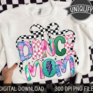 May include: White sweatshirt with a colorful graphic design that says "Dance Mom". The design features a checkered bow, floral patterns, and a lightning bolt.