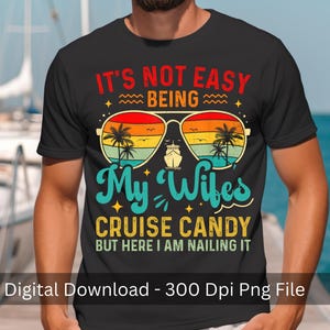 May include: Black t-shirt with a colorful graphic design. The design features sunglasses with a sunset scene, palm trees, and a cruise ship. Text includes "IT'S NOT EASY BEING My Wifes CRUISE CANDY BUT HERE I AM NAILING IT."