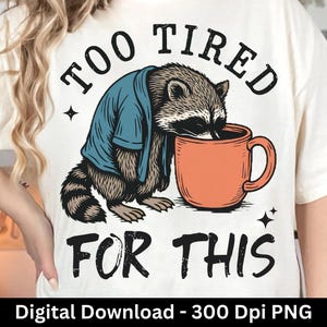 Op de afbeelding: Cr&egrave;mekleurig T-shirt met een afbeelding van een wasbeer in een blauw shirt, leunend op een oranje mok. De tekst "TOO TIRED FOR THIS" staat boven en onder de wasbeer. De onderkant van de afbeelding luidt "Digital Download - 300 Dpi PNG".