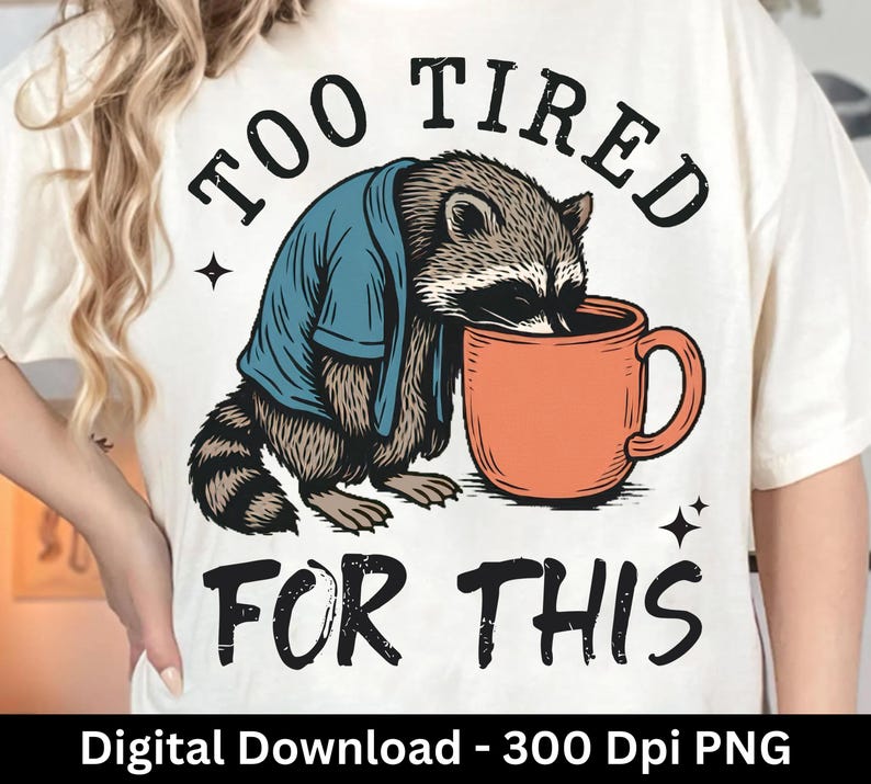 Op de afbeelding: Cr&egrave;mekleurig T-shirt met een afbeelding van een wasbeer in een blauw shirt, leunend op een oranje mok. De tekst "TOO TIRED FOR THIS" staat boven en onder de wasbeer. De onderkant van de afbeelding luidt "Digital Download - 300 Dpi PNG".