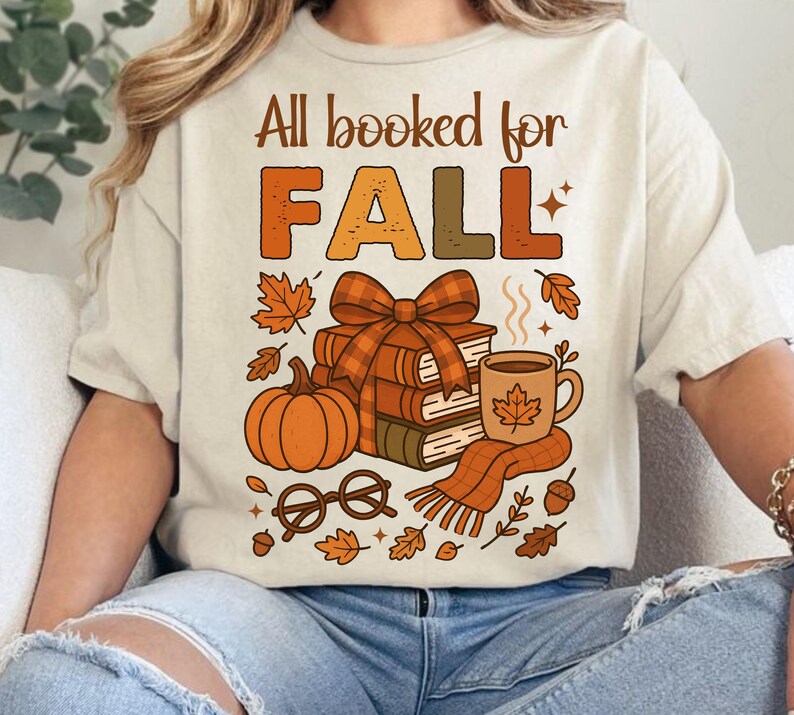 May include: Beige t-shirt with the text "All booked for FALL" in orange and brown. The graphic includes a pumpkin, books, a coffee mug, and fall leaves. A cozy autumn-themed design.