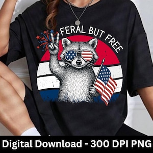 以下が含まれることがあります： アメリカ国旗のデザインのサングラスをかけたアライグマがピースサインをし、小さなアメリカ国旗を持っている黒いTシャツ。アライグマの上には「FERAL BUT FREE」の文字。