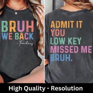 K&ouml;nnte beinhalten: Dunkelgraues T-Shirt mit farbenfrohem Text. Auf der Vorderseite steht "BRUH WE BACK - Teachers." Auf der R&uuml;ckseite steht "ADMIT IT YOU LOW KEY MISSED ME BRUH." Der Text ist in Orange, Pink, Blau und Gr&uuml;n.
