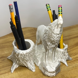 Peut inclure: Organiseur de bureau en céramique blanche avec une sculpture de loup et deux porte-crayons en forme de souche d'arbre. Le loup hurle et se tient sur une base. Les porte-crayons sont texturés pour ressembler à des souches d'arbres.