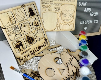 May include: A Halloween craft kit with wooden pieces to build a monster, a skull, and other spooky shapes. The kit includes paint, a paintbrush, and twine. The box is white with the words "Greyson's Tic-Tac-Halloween" printed on it. The kit is made by Oak and Iron Design Co.