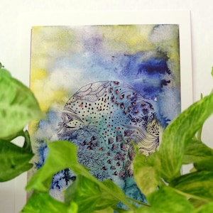 May include: Watercolor painting with a blue, yellow, and purple background. The artwork features a detailed, circular design with floral and abstract patterns in black and pink. The painting is framed in white.