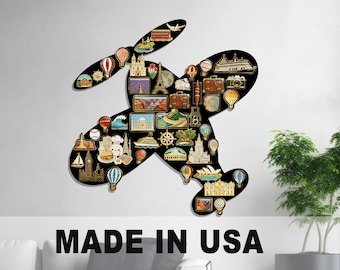 May include: Black airplane-shaped wall decor filled with travel-themed pins. The pins feature landmarks, hot air balloons, and luggage. The text "MADE IN USA" and "SHIP IN 48 HOURS" are at the bottom.