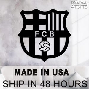 May include: Black metal wall art featuring the FC Barcelona crest. The design includes the letters "FCB" and a soccer ball. The wall art is displayed against a neutral background.