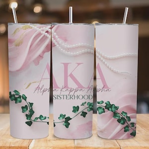 May include: A pink tumbler with a floral design, pearl accents, and the text "AKA Alpha Kappa Alpha SISTERHOOD." The tumbler features a straw and a green ivy design.