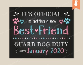 May include: A black chalkboard sign with white text announcing "It's Official I'm getting a new Best Friend" with pink and blue paw prints. The sign also states "Guard Dog Duty starts January 2020".