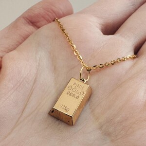 May include: A gold chain necklace with a gold bar pendant that reads "FINE GOLD 999.9 1Kg".