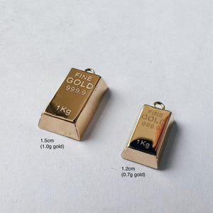 May include: Two gold-colored bars with "FINE GOLD 999.9" and "1Kg" printed on them. The larger bar is 1.5 inches (1.0g gold) and the smaller bar is 1.2 inches (0.7g gold).