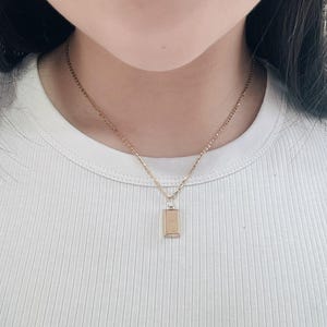 May include: A gold chain necklace with a small rectangular pendant. The pendant is 1.2 cm long.