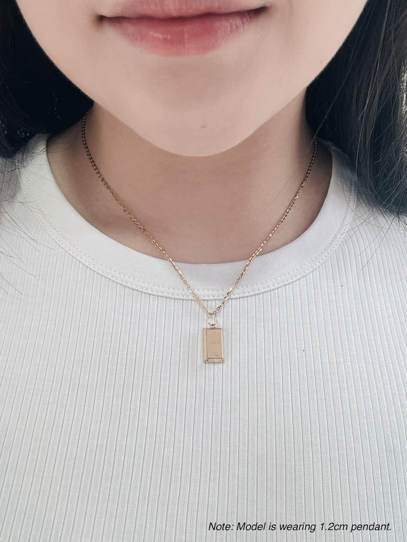May include: A gold chain necklace with a small rectangular pendant. The pendant is 1.2 cm long.