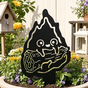 May include: A black metal garden stake featuring a cutout design of a small, round, smiling creature with large eyes holding a horizontal log. The silhouette of the creature is surrounded by a flame-like shape, and the log has etched details.