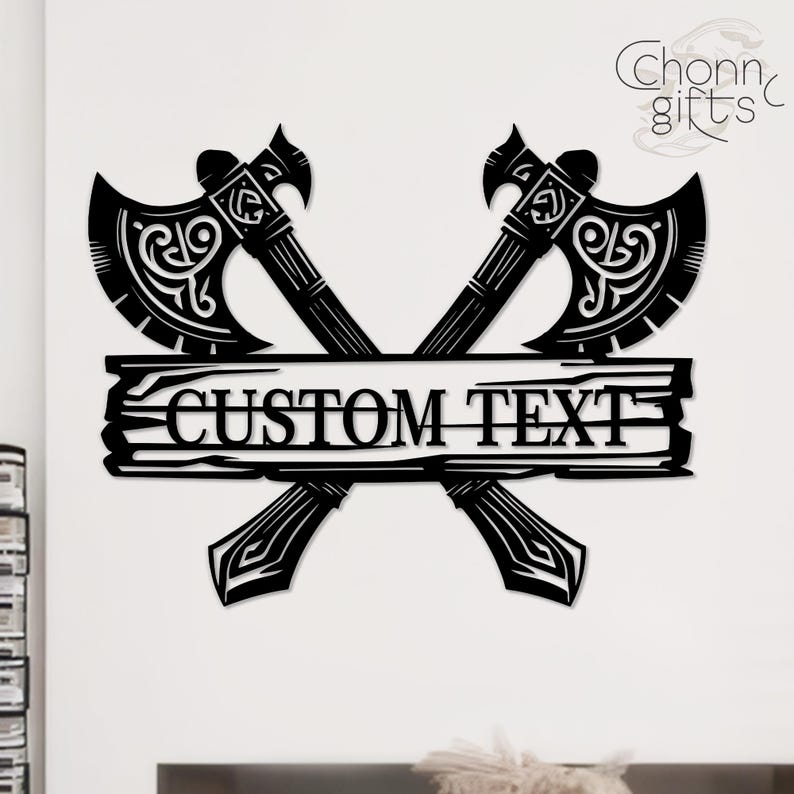 May include: Black metal wall art featuring two crossed axes with ornate detailing. A wooden plank in the center displays the text "CUSTOM TEXT". The design includes decorative elements and the brand name "Chonn gifts".
