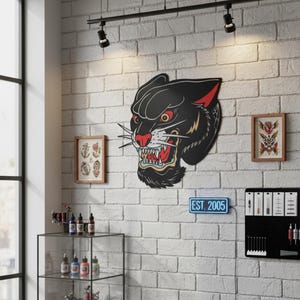 Könnte beinhalten: Schwarze Pantherkopf-Wandkunst mit roten und gelben Akzenten, montiert an einer weißen Backsteinmauer. Der Panther hat ein offenes Maul mit sichtbaren Zähnen. Die Wand zeigt auch gerahmte Kunst und ein Neonschild mit der Aufschrift "EST. 2005."