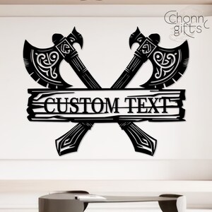May include: Black metal wall art featuring two crossed axes with ornate detailing. A wooden plank with the words "CUSTOM TEXT" is centered between the axes. The design includes the text "Chonn gifts" in the upper right corner.